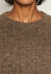 Maglione di lana marrone con scollo rotondo; presenta un aspetto morbido e testurizzato con diverse sfumature di marrone nel tessuto.