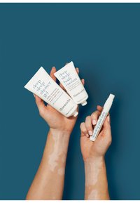 Kolme valkoista putkea thisworks-tuotteista: "deep sleep shower gel", "deep sleep body cocoon" ja "deep sleep pillow spray", pidetään kahdessa kädessä.