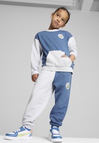 Sudadera a rayas en azul y gris con un bolsillo delantero y un logo, combinada con pantalones de chándal a juego y zapatillas deportivas azules con colores de acento.