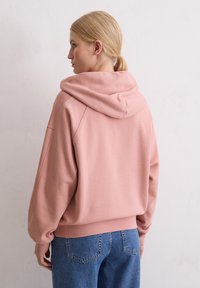 Różowa bluza z kapturem o luźnym kroju, z prążkowanymi mankietami i dołem. Materiał wydaje się miękki o gładkiej fakturze.