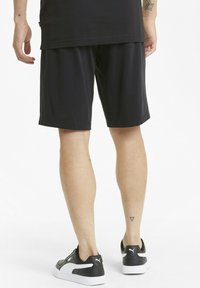 Shorts sportivi neri con vita elastica, taglio dritto e trama liscia, abbinati a scarpe da ginnastica nere e bianche.