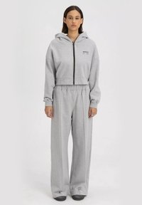 Grijze cropped hoodie met rits en trekkoord, gecombineerd met losse grijze joggingbroeken. Beide zijn gemaakt van zachte, gestructureerde stof.