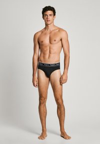 Schwarze Unterhosen mit einem taillierten Design und einem weißen Markenschriftzug am Bund. Der Stoff wirkt glatt und elastisch, geeignet für komfortables Tragen.