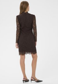 Pruuni pitskleit pikkade varrukatega, kõrge kaelusega ja sakilise äärega. Omab kehakujundavat siluetti ja diskreetseid lillemotiive.