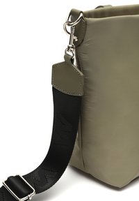 Olivovo zelená nylonová taška s textúrovaným povrchom, vybavená čiernym popruhom s embosovaným logom a strieborným kovovým hardvérom na pripojenie.