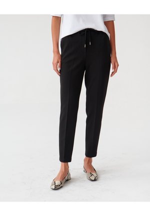 Zwarte tapered broeken met een trekkoord in de taille, gemaakt van een gladde stof. Gecombineerd met gemusterde platte schoenen met een slangenhuidontwerp.