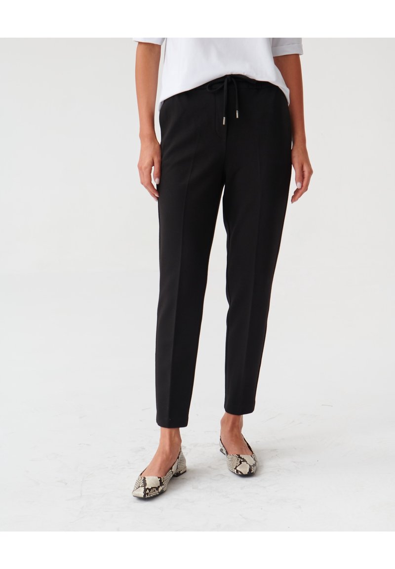 Svarta smala byxor med dragsko i midjan, tillverkade av ett smidigt tyg. I kombination med mönstrade, platta skor med ormskinnsdesign.