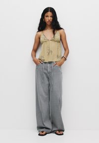 Top halter galben deschis cu broderie florală, asortat cu pantaloni largi gri deschis și sandale negre. Design minimalist.