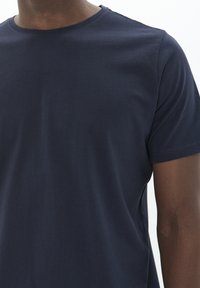 Camiseta de algodón de color azul marino con cuello redondo y mangas cortas. Textura suave, diseño ajustado y costuras mínimas en los hombros.