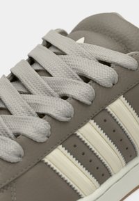 Γκρι δερμάτινο αθλητικό παπούτσι με ανοιχτό γκρι κορδόνια, που διαθέτει τρεις λευκές ρίγες στο πλάι και υφή στη σόλα χρώματος καραμέλας.