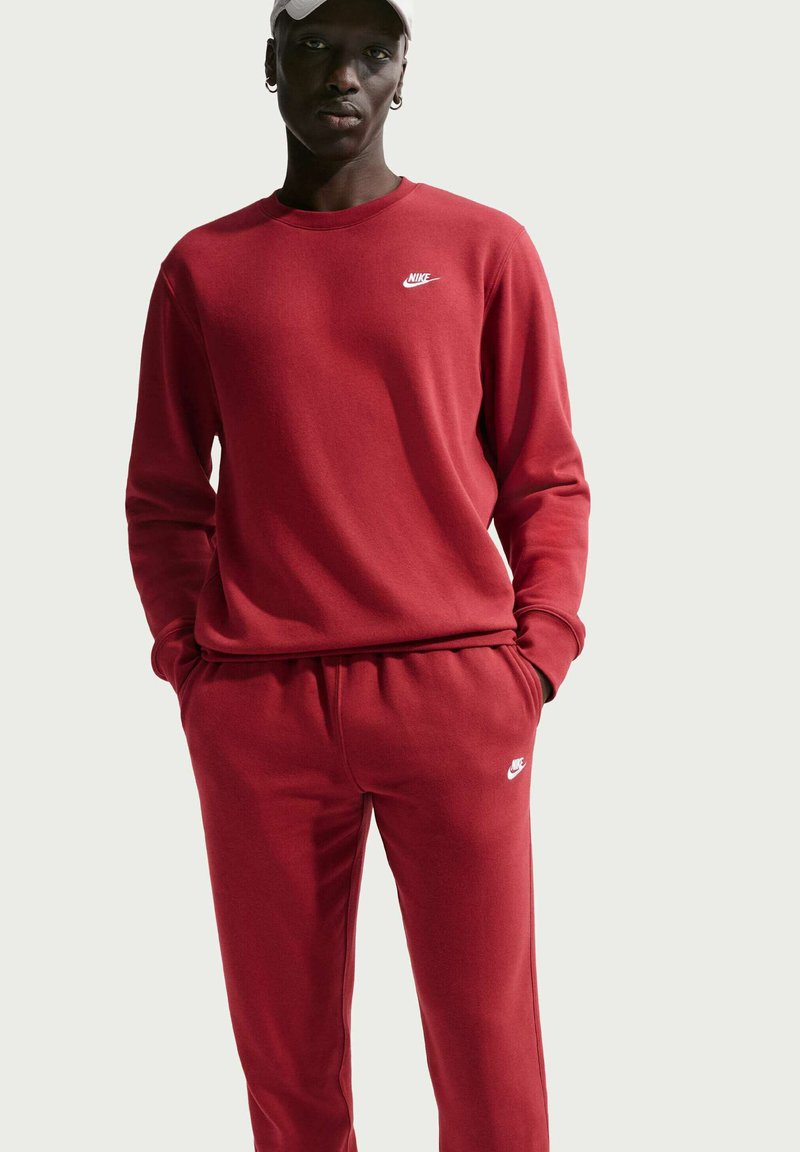 Felpa rossa Nike con pantaloni jogger abbinati, realizzati in tessuto morbido. La felpa presenta un collo rotondo e un logo; i jogger hanno una vita elasticizzata.