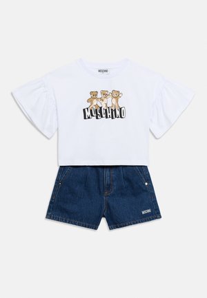 Bela kratka majica s tremi medvedki in napisom "Moschino", kombinirana z visokim pasom temno modrih kavbojskih kratkih hlač z logotipom na robu.