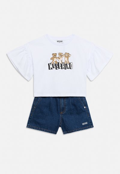 Fehér, rövidített fazonú póló három macival és "Moschino" felirattal, magas derekú sötétkék farmer rövidnadrággal párosítva, amelynek szegélyén logó található.