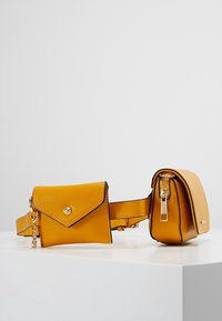 Belt bag gialla in finta pelle con due scomparti; uno presenta una pattina con bottone a scatto, l'altro ha una chiusura con zip. Superficie texture.