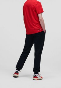 Rød kortærmet t-shirt kombineret med sorte bukser, der har en afslappet pasform. Skoene er hvide med røde og gyldne detaljer.