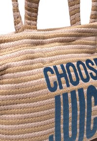 Torebka typu tote wykonana z tkaniny w beżowo-różowe paski z niebieskim napisem "CHOOSE JUICE". Solidny, teksturowany materiał z dwoma uchwytami do noszenia.