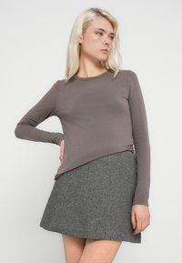 Bluza maro, cu mâneci lungi și croială strâmtă, asortată cu o fustă gri în model chevron. Ținuta are o textură netedă și un design simplu.