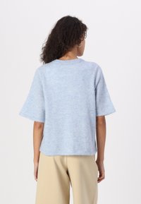 Pull léger bleu clair à manches courtes avec une texture douce et moelleuse. Doté d'un col rond et d'une coupe décontractée, il est associé à un pantalon large beige.