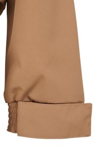Brown jacket cuff with gathered elastic detail, smooth texture, and a clean seam finish. Fabric appears water-resistant and durable.