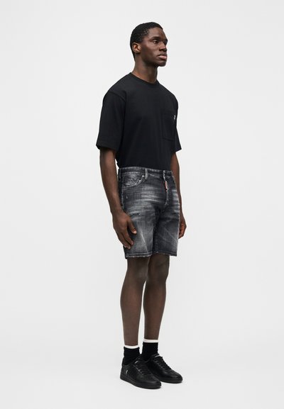 Črna majica s kratkimi rokavi in žepom, kombinirana s svetlo sivimi denim kratkimi hlačami z razpokanimi robovi in nežnim obrabljanjem. Oblečeno s črnimi supergami.