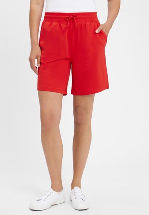Red sweat shorts with an elastic waistband and drawstring, featuring side pockets and a relaxed fit. Worn with white sneakers.