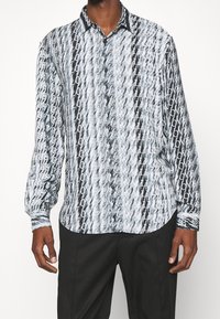 Camicia a maniche lunghe con bottoni, caratterizzata da un motivo astratto bianco e nero con design di testo ripetuto e colletto standard. Tessuto morbido al tatto.