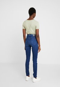 Mörkblå high-waisted jeans i denim med en mjuk textur, tillsammans med en ljusgrön kortärmad skjorta och vita sneakers.