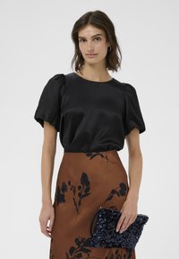 Bluză din satin negru cu mâneci bufante, asortată cu o fustă maro cu model floral. O geantă de sequin albastră completează ținuta.