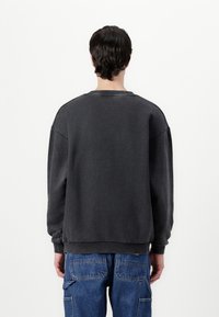 Gray oversized sweatshirt with a crew neck, ribbed cuffs, and hem. Made of soft material with a slightly textured finish.