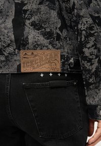 Μαύρο τζιν από τζιν με υφή και γκρι σακάκι με λουλουδάτο μοτίβο. Διαθέτει δερμάτινη ετικέτα ICECREAM και διακριτικές λευκές ραφές.