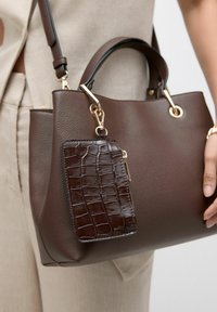 Braune Lederhandtasche mit strukturiertem Finish, ausgestattet mit einem abnehmbaren, dunkelbraun geprägten Geldbeutel und goldenen Hardware-Details.