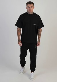 Musta ylivuotoinen t-paita, jossa pyöreä pääntie, yhdistetty mustiin vetoketjulla varustettuihin joggereihin ja valkoisiin lenkkareihin, joissa on teksturoidut pohjat.