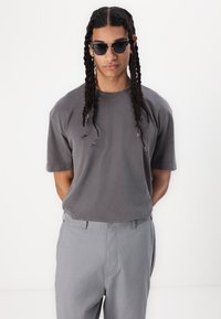 Gray oversized t-shirt with short sleeves, paired with light gray trousers. The t-shirt has subtle distress details and a relaxed fit.