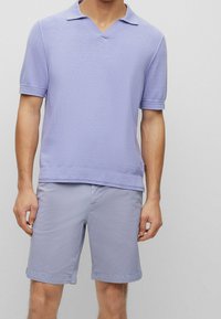 Man wearing a light purple short-sleeve knit polo shirt and matching purple knee-length shorts against a plain background.