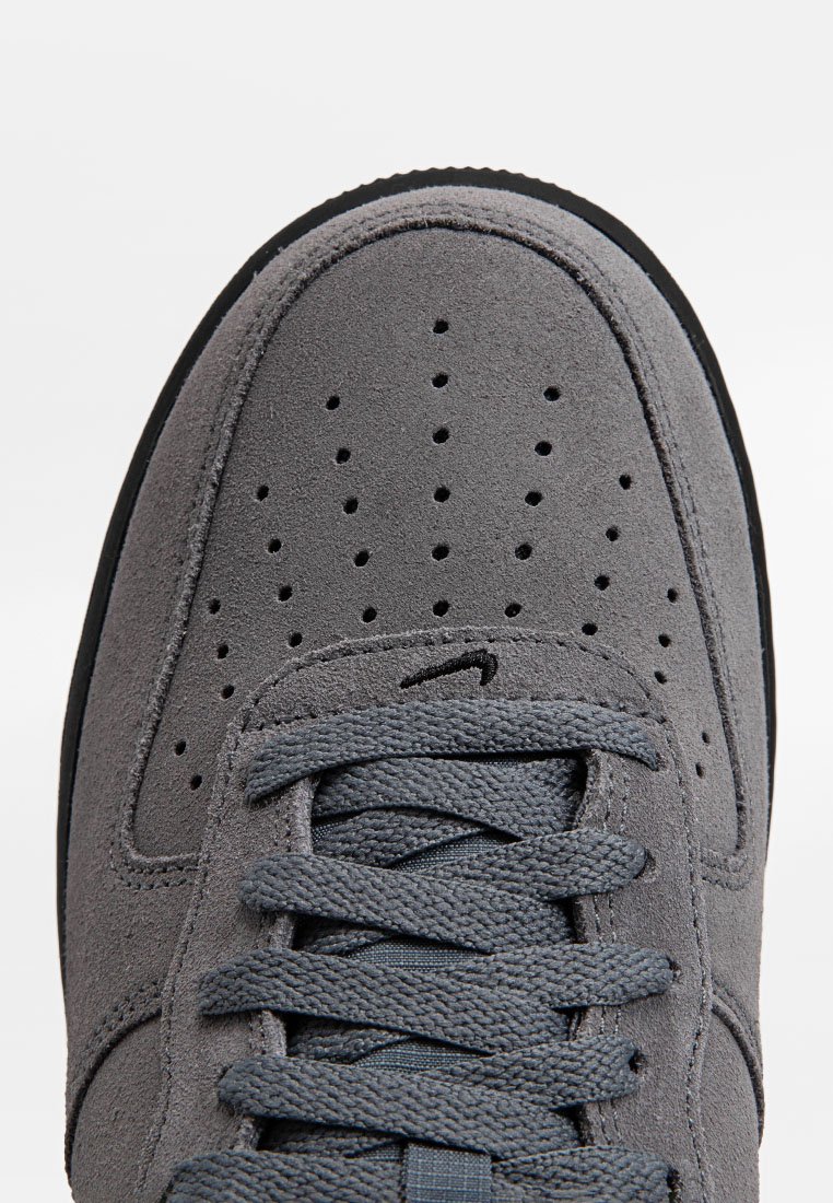 Zapatillas de ante gris con puntera perforada, cordones planos grises y suela de goma negra contrastante. Presenta un sutil logotipo de la marca.