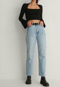 Svart långärmad crop top med fyrkantig halsringning; ljusblå högmidjade jeans; svarta chunky ankelskor med texturerad sula.