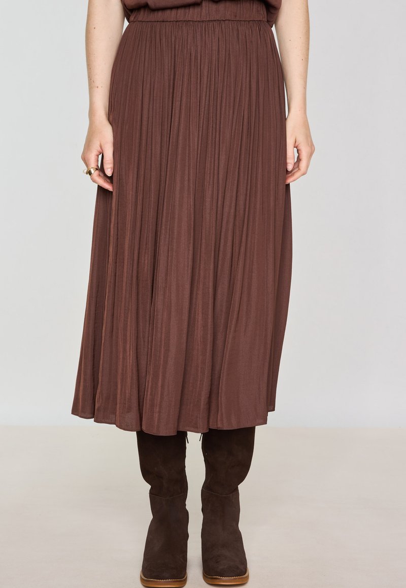 Gonna midi plissettata marrone con vita elastica, realizzata in tessuto morbido, abbinata a stivali marroni in suede al ginocchio.