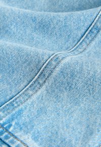 Tissu en denim bleu clair avec un tissage diagonal visible et des coutures double piqûre en fil beige.