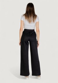 Pantalones anchos negros con una cintura alta, que presentan un sutil patrón texturizado. Combinados con una blusa blanca de manga corta ajustada.