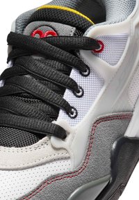 Sneaker z szarym zamszem i materiałem meshowym, czarnymi sznurówkami, białymi perforowanymi panelami, czerwonymi akcentami i żółtym kołnierzem. Teksturowana gumowa podeszwa.