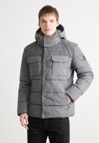 Giacca puffer grigia con parte superiore in tessuto a coste, due tasche sul petto, bottoni a pressione e cappuccio regolabile, con una texture trapuntata su tutta la giacca.