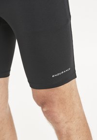 Svarta sportshorts tillverkade av elastiskt tyg, med en tät passform och varumärket "ENDURANCE" tryckt i vitt på underbenet.