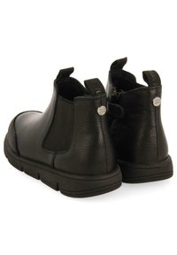 Botas de tobillo de cuero negro con paneles laterales elásticos y tiradores. Presentan una superficie texturizada y una suela ligera y flexible.