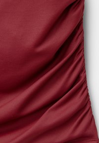 Gros plan sur un tissu rouge profond et lisse avec des détails froncés et plissés sur le côté droit créant des plis texturés.