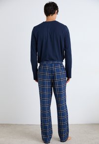 Cămașă cu mânecă lungă de culoare bleumarin și pantaloni de pijama în carouri albastre, cu linii albe în grilă, talie elastică și croială lejeră. Materialul texturat este prezentat.