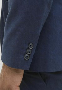 Ärmel einer marineblauen Anzugsjacke mit glatter Textur, ausgestattet mit vier schwarzen Knöpfen und genähten Details. Nahaufnahme des Manschettenbereichs.