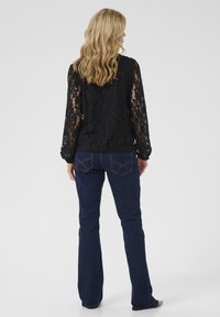 Blusa nera in pizzo con maniche lunghe abbinata a jeans a campana blu scuro. I dettagli notevoli includono la texture in pizzo e le cuciture sui jeans.