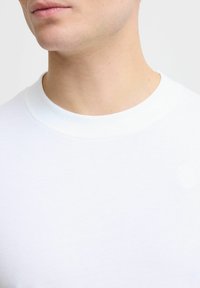 Hvid crew-neck t-shirt lavet af blødt bomuldsstof. Har en glat tekstur med et lille logodetalje på venstre brystområde.