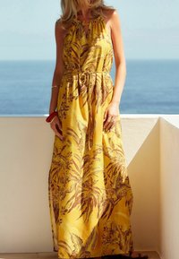 Robe maxi jaune avec motifs floraux et feuilles marron, design sans manches, lien ajustable à la taille, tissu fluide, texture lisse.