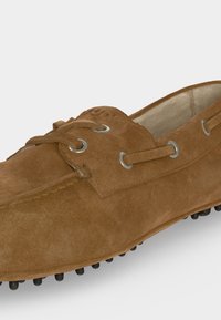 Mocassin en daim marron avec détails lacets, œillets métalliques et semelle en caoutchouc à picots pour adhérence et confort.